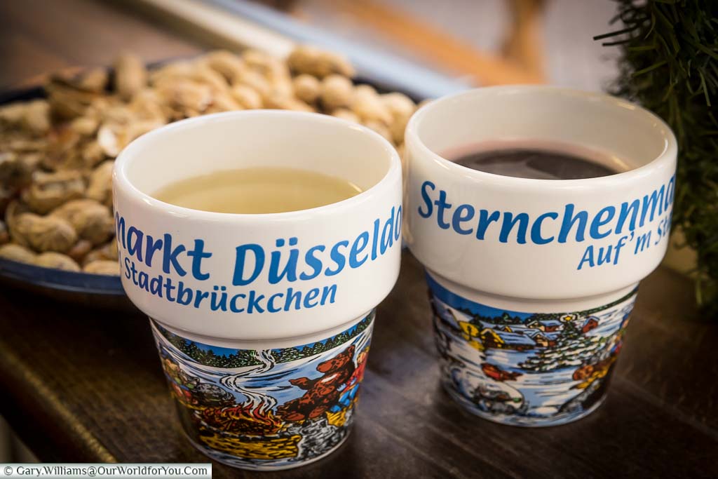 Two mugs of red & white Gluhwein served with a plate of monkey nuts in Düsseldorf Christmas Markets
