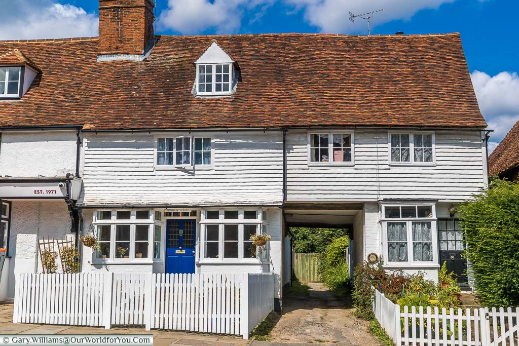 White picket fences in front of two traditional white weather boarded Kentish homes With the red tiled roof. There is a driveway running between them wide enough for possibly a horse and cart.