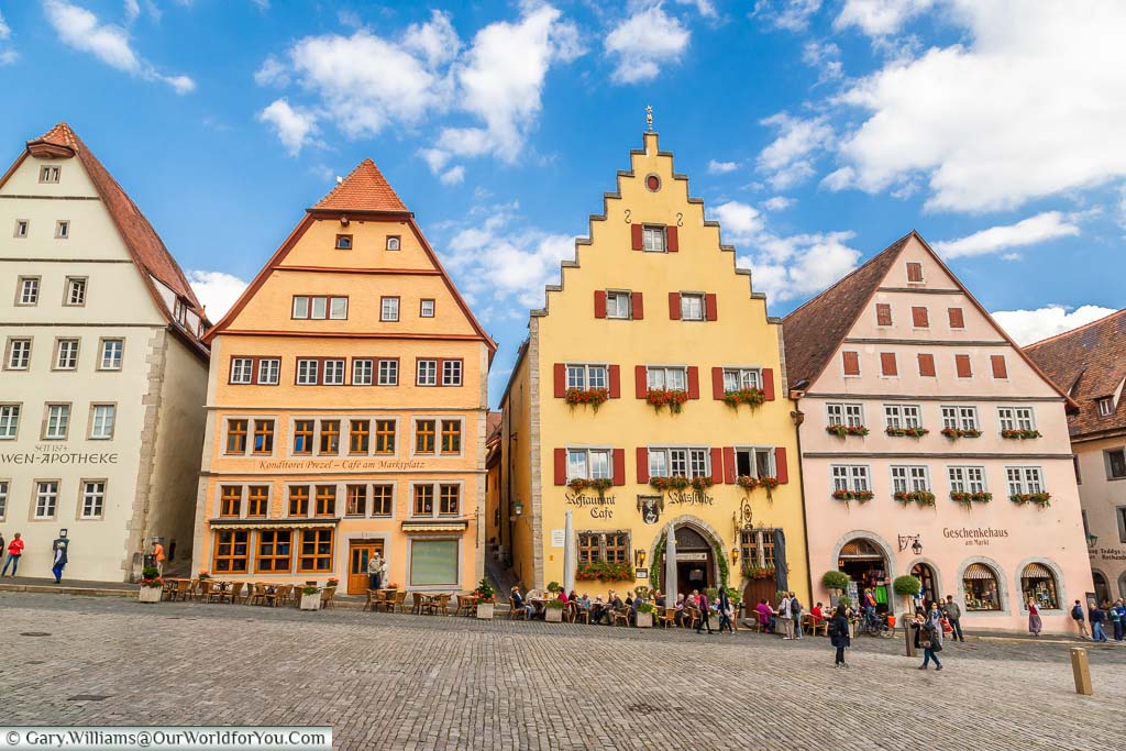 A selection of typical buildings lining Marktplatz in Rothenburg ob der Tauber. Each building is in a different muted colour, with shop signs in a uniform script font.