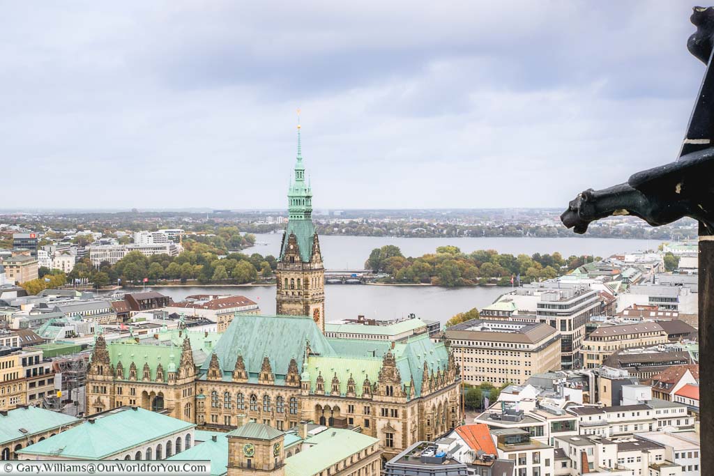 A view from the neo-gothic St Nikolai-church tower across the Rathaus to the been Binnenalster and beyond. On the right of the frame is a gargoyle, part of the tower structure.