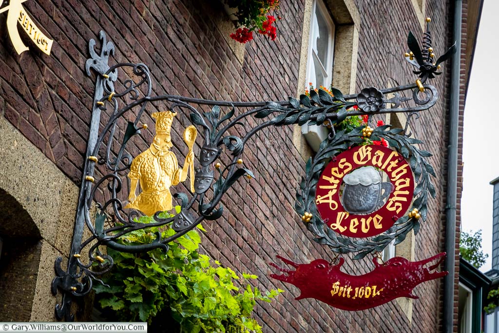 The wrought iron sign of Altes Gasthaus Leve. The restaurant sign depicts a chef with a wooden sport.