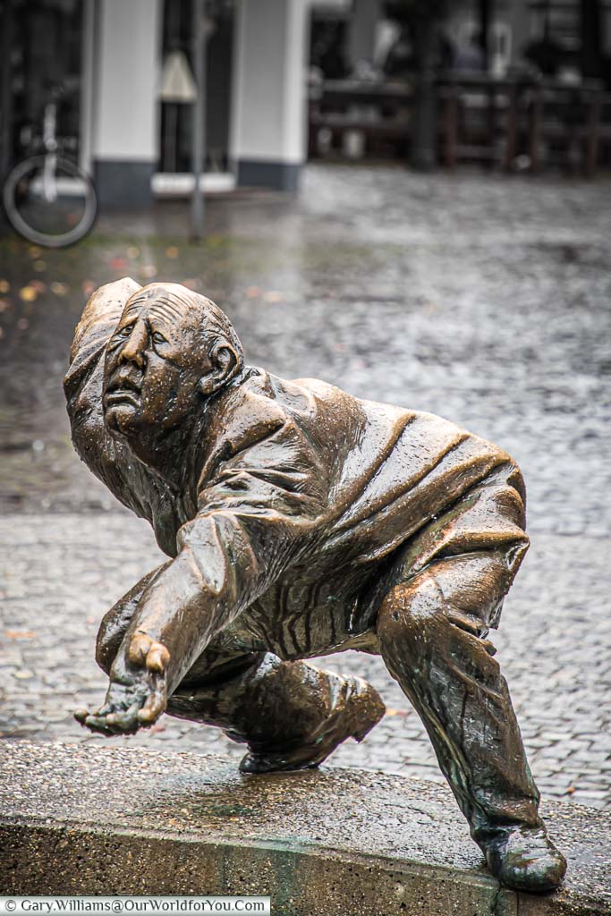 A brass statue of old man, bent over, hand out, begging for loose change next to Circle of Money fountain.