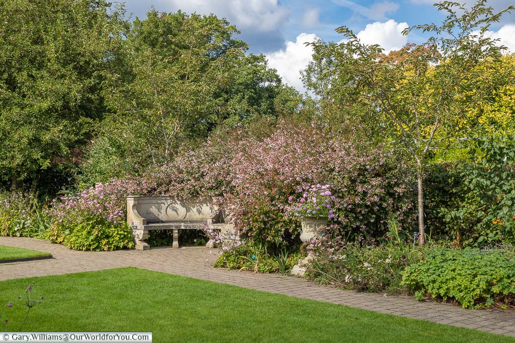 A stone, semi-circular, bench at the far end of the Cottage Garden in amongst the pink flowers of the border.