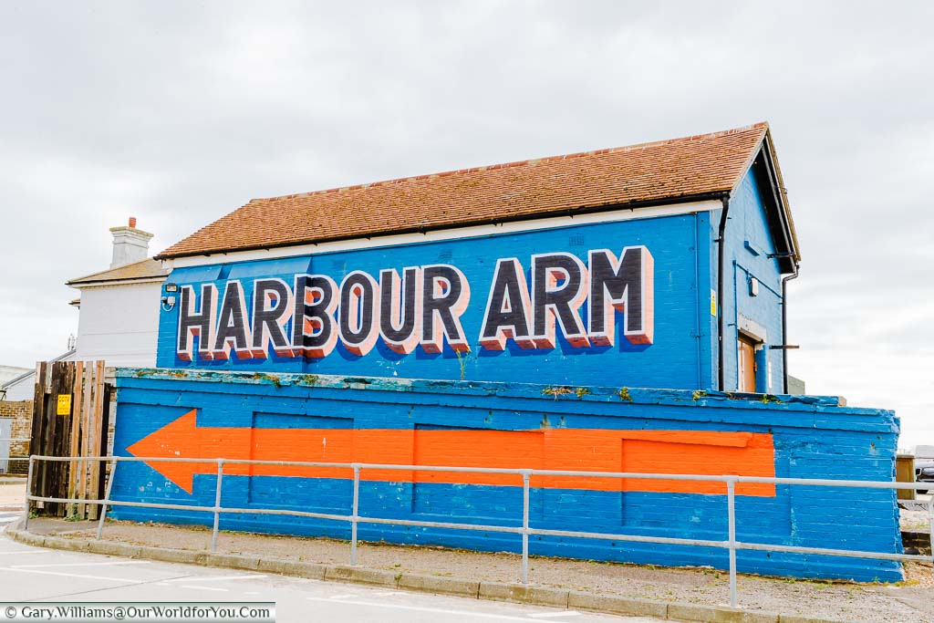 A blue brick building with a bright orange arrow and labelled Harbour Arm,