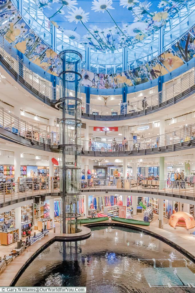 A wide-angle portrait shot of the central atrium inside of the Globetrotter store. The view extends from the daisy covered blue sky through 4 stories down to the pool at the bottom of the store.