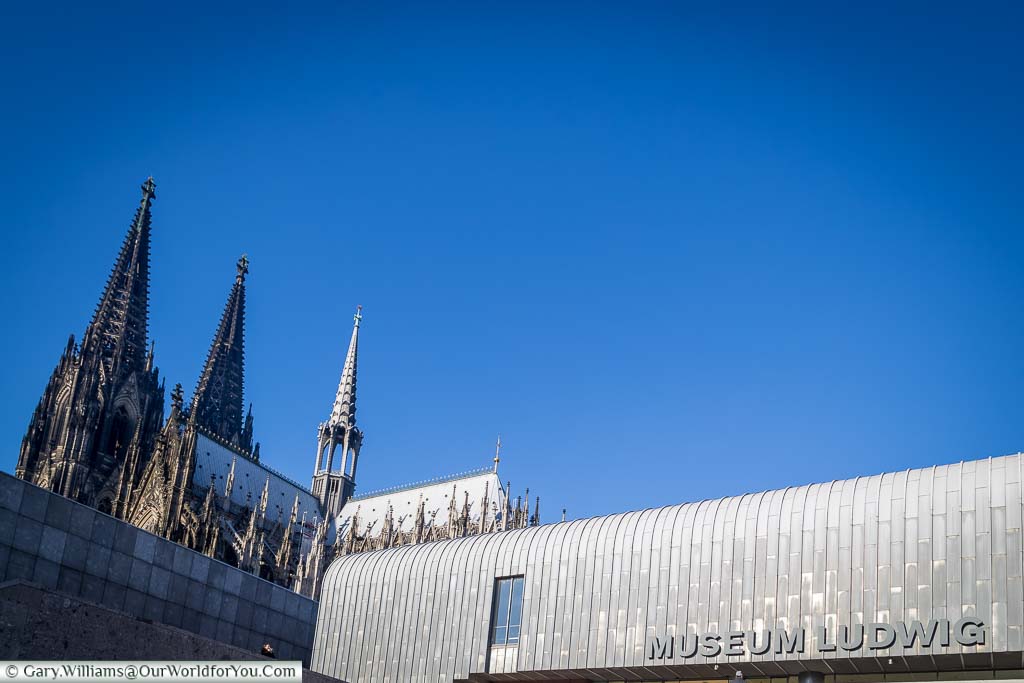 A shot of the silvery aluminium roof of Museum Ludwig with Cologne's cathedral in the background set against a deep blue sky.