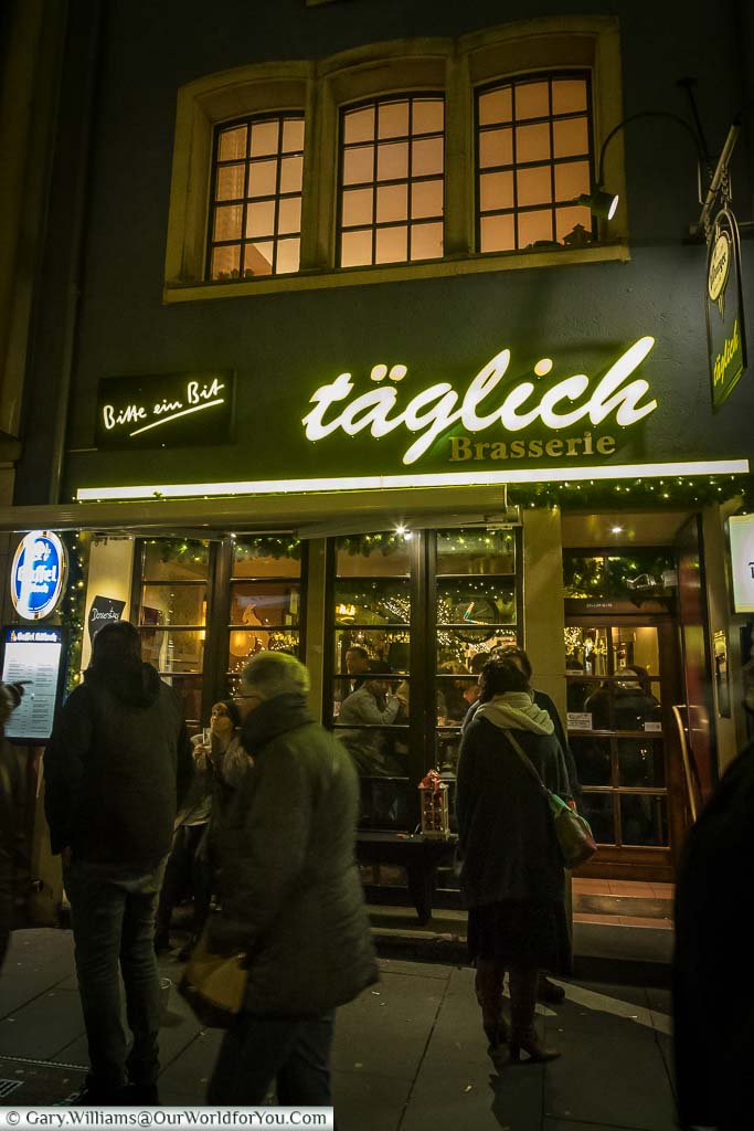 People strolling past the Täglich Brasserie. The narrow front of the shop hides the depth of the building, and its long bar.