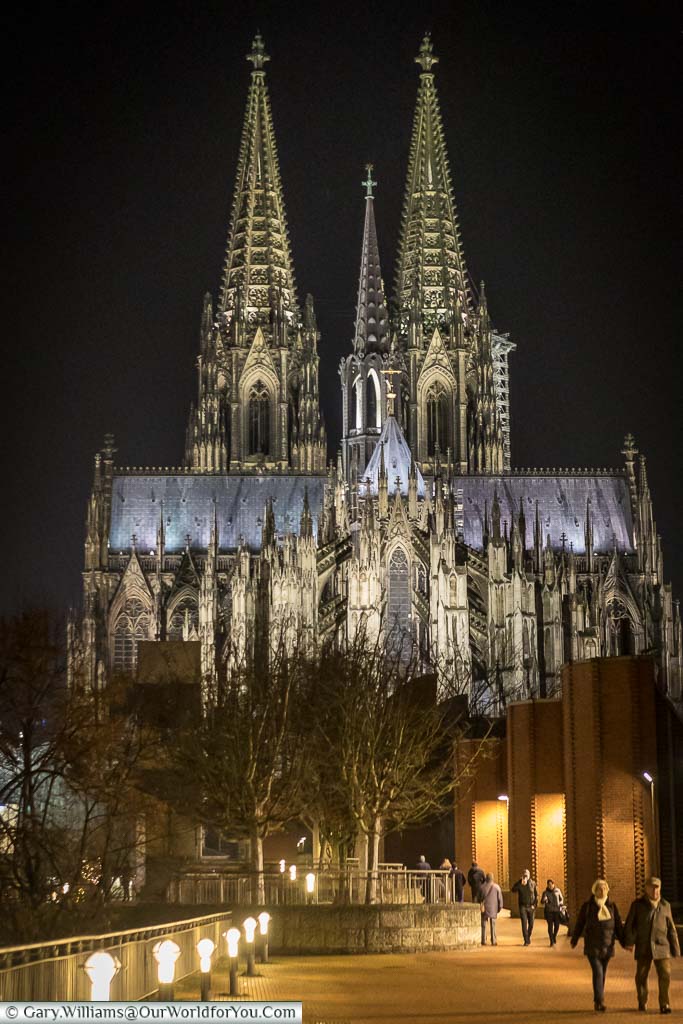 A view of Cologne cathedral in the evening from the east after just crossing the Hohenzollernbrücke bridge. The cathedral is beautifully floodlit and looks stunning against the dark sky.