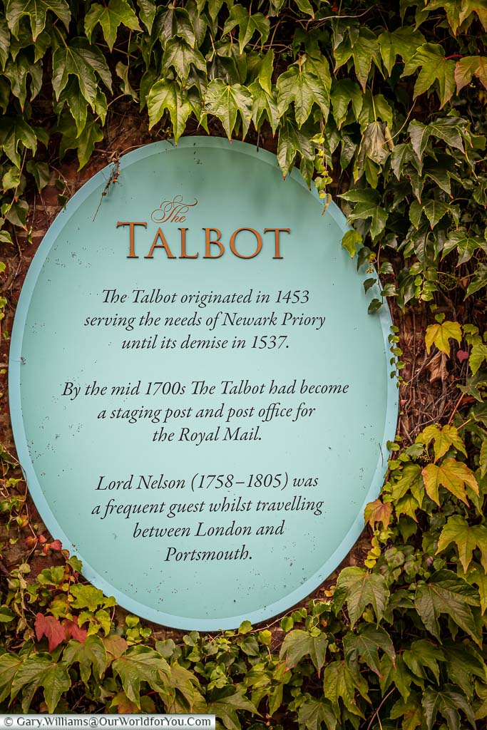 A plaque mounted on the external wall of The Talbot Inn detailing its history through time.