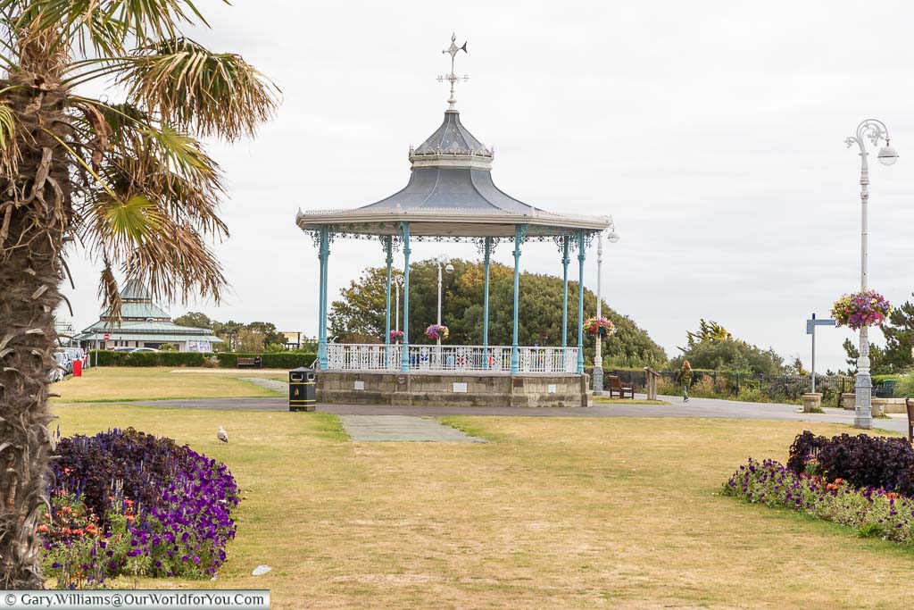 An ornate Victorian bandstand with aqua coloured pillars supporting its grey roof on the Leas promenade.