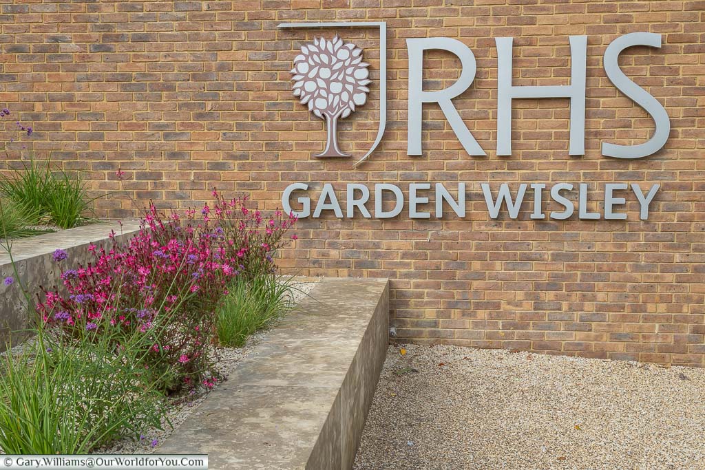 The RHS Garden Wisley sign mounted on a brick wall at the entrance to the gardens.
