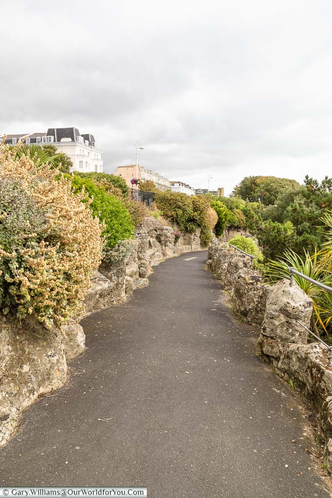 A tarmac path heading down through a man-made rocky landscape that leads towards the beach.