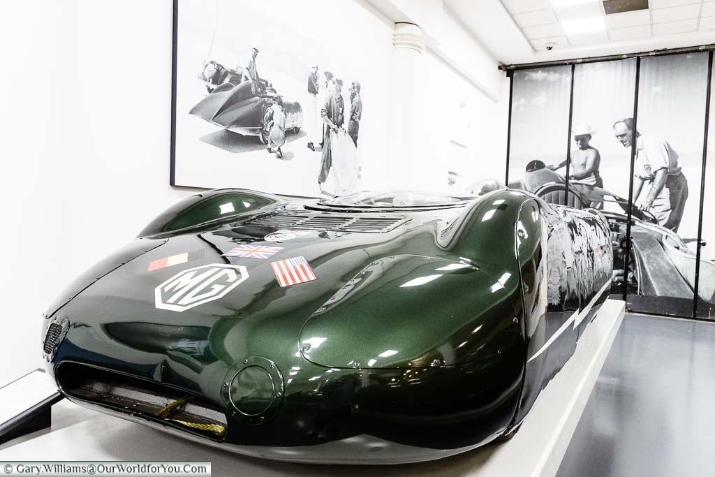 A streamlined car with an MG badge in a metallic British racing green, designed to tackle the Land Speed record, on display in British motor museum.
