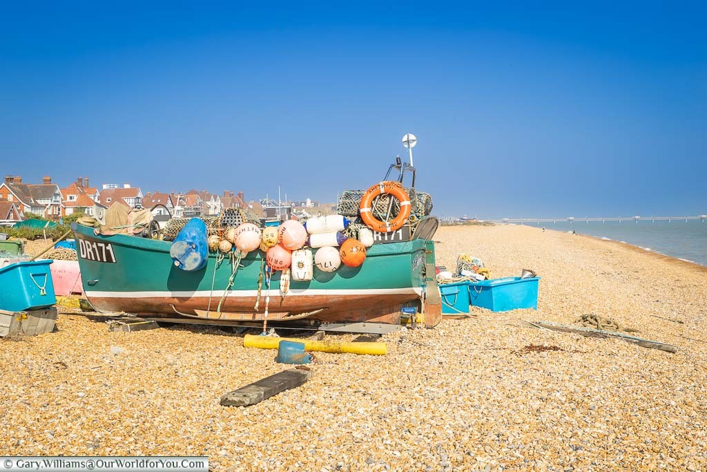 A small fishing boast surrounded by and covered in, floats and other fishing paraphernalia on the beach in Deal, Kent