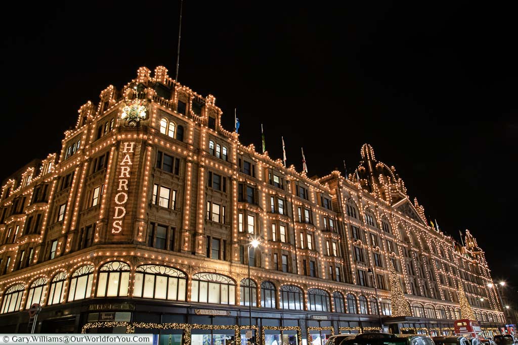 A side view of the Harrods Department store decorated with hundreds of small lights and a pair of Christmas trees above the main entrance.