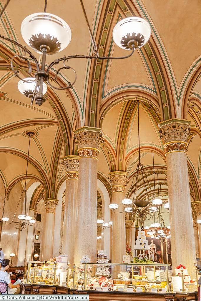 Inside the elegant Café Central in Vienna with it's high vaulted ceiling and decorative lighting. In front of us is a pastry counter serving the elegant patisseries these cafés are renown for.