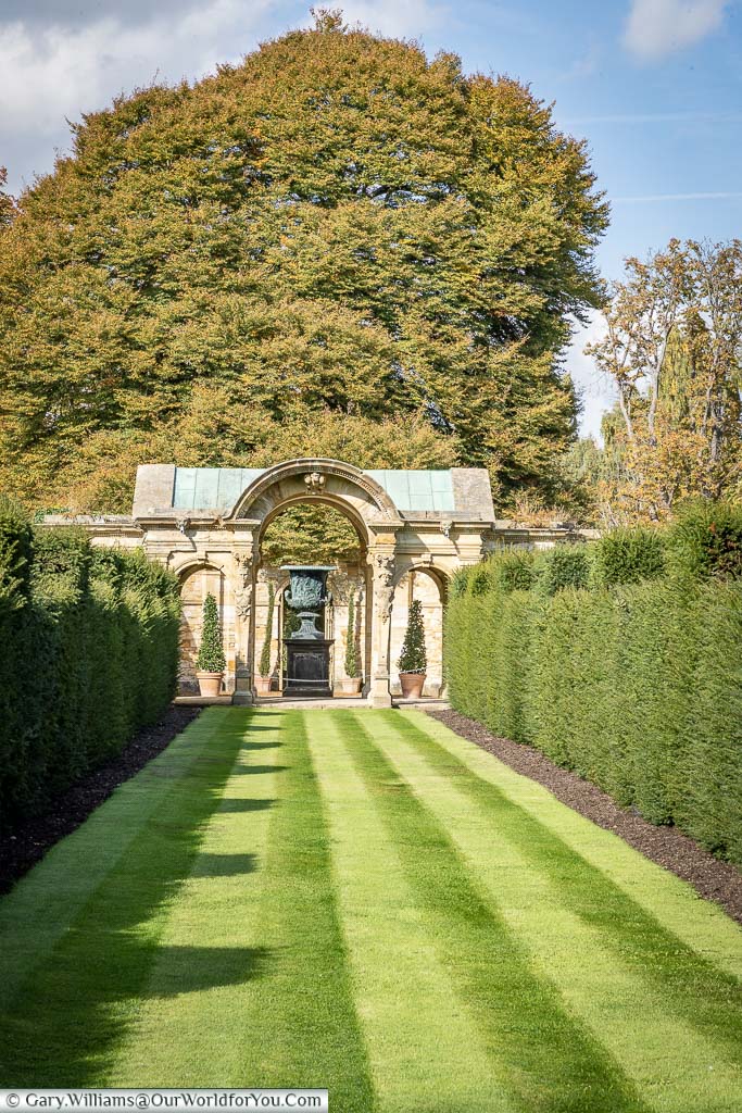 A strip of beautifully manicured lawn leading to a stone arch in the Italian Garden at Hever Castle