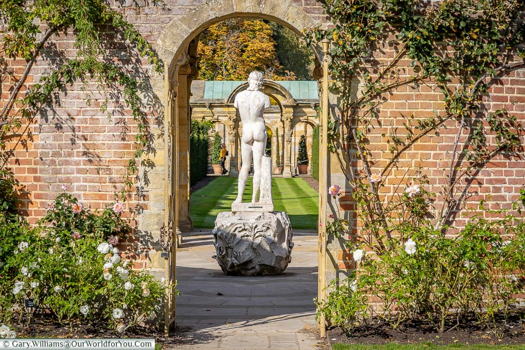 A view through the arch Rose Garden to the back of a marble statue of an athletic man in the Italian Garden at Hever Castle