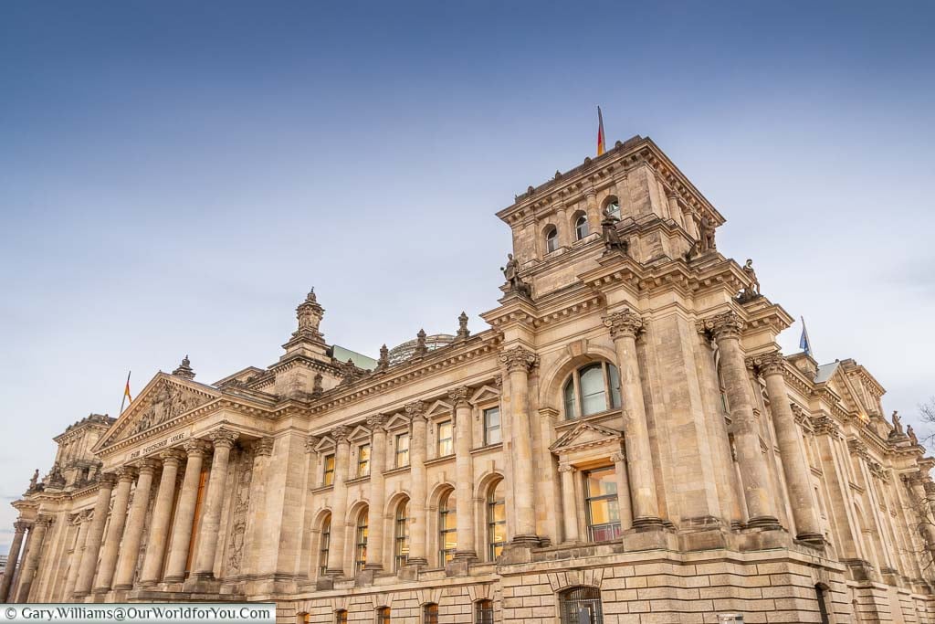 The grand neoclassical building that is the Reichstag. tinged with an orange glow as dusk sets in.