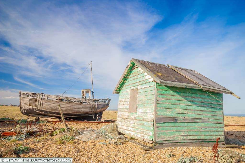 A small decaying wooden fishing boat next to a fisherman's hut on the shingle beach of Dungeness