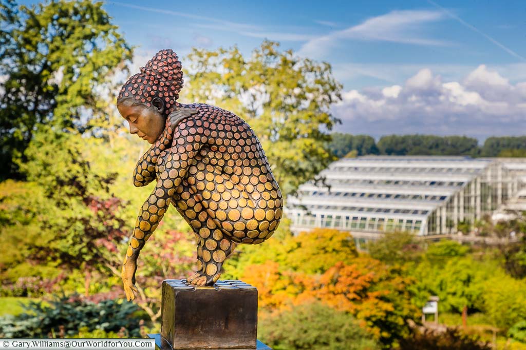 A modern art statue called 'Sunset' by Jonathan Hately on a plinth in the grounds of RHS Wisley with the Glasshouse in the background