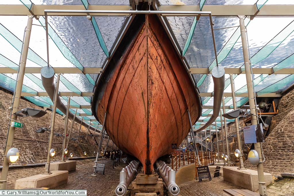 In the dry dock of the Great Western Dockyard looking at the bow of the SS Great Britain under cover of glass with a thin layer of shimmering water