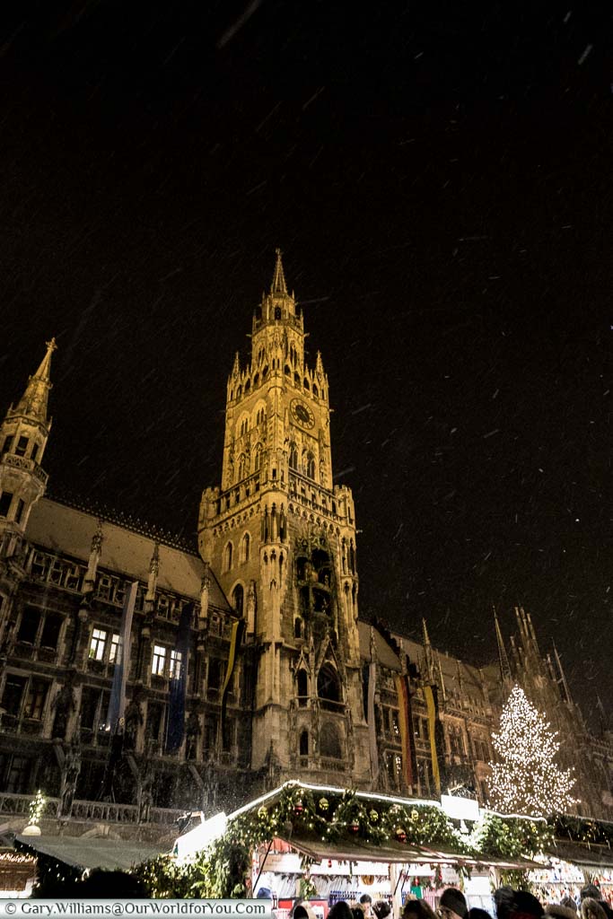 Looking up at the tower of Munich's Rathaus with markets stalls below as snow falls.