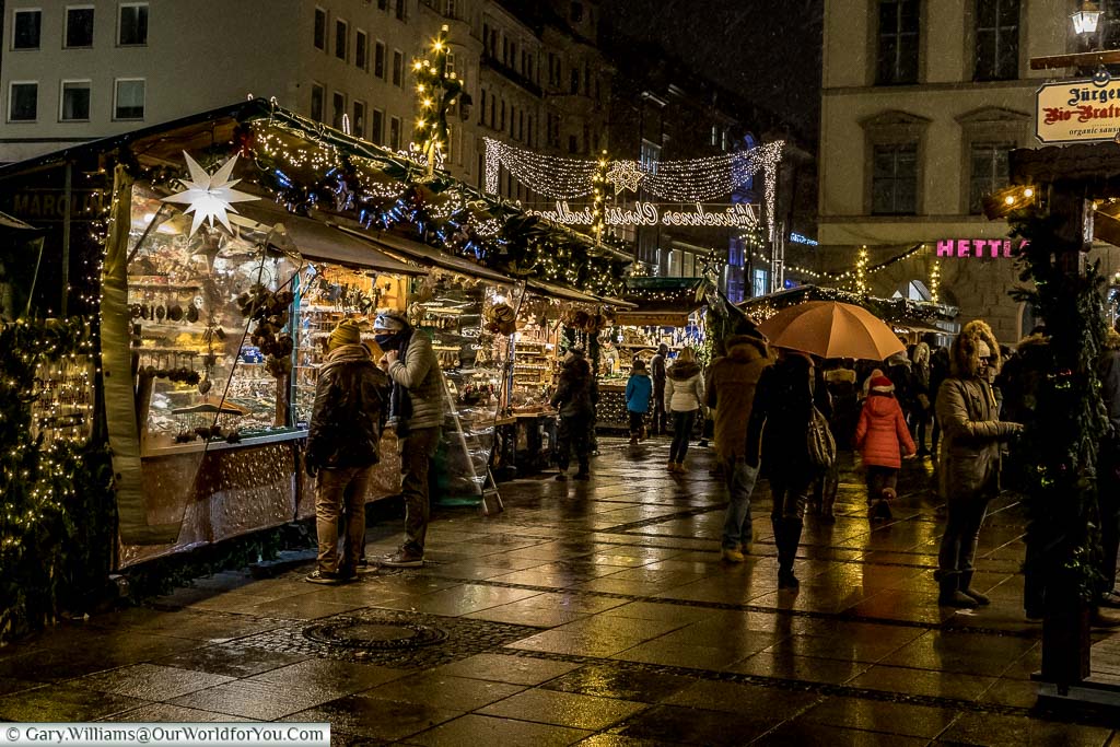 A collection of huts on the edge of one of Munich's Christmas markets as it drizzles and the pavement glistens.