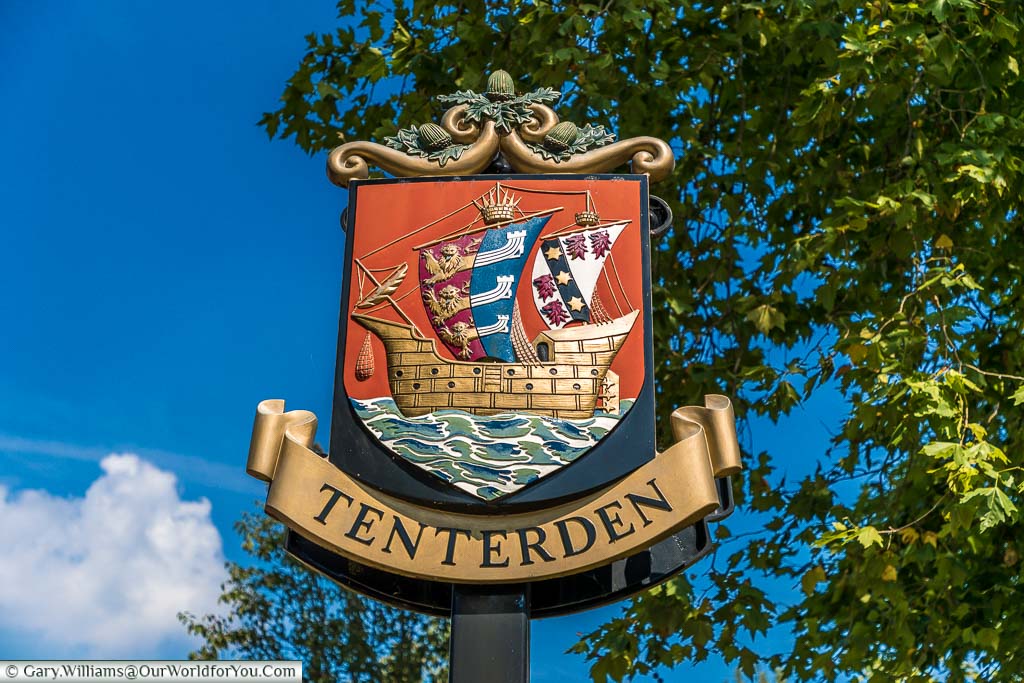 The Tenterden town sign depicting a galleon on the open sea with sails displaying the coat of arms of the cinque ports which are 3 heraldic lions that merge into 3 long boats.