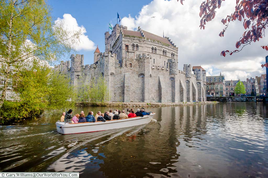 A small tourist boat passes in front of the stone Castle of the Counts in Ghent, Belgium