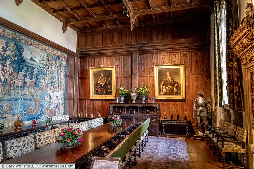 The dining hall of Hever Castle, with a large central table, a tapestry on one wall and portraits on another oak panelled wall.