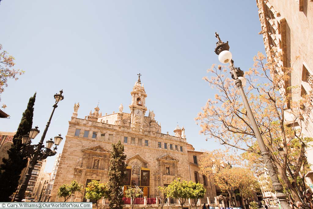A beautifully ornate church in central Valencia distinguished with a triangular Bell tower, topped with statues of Saints on a golden spring day.