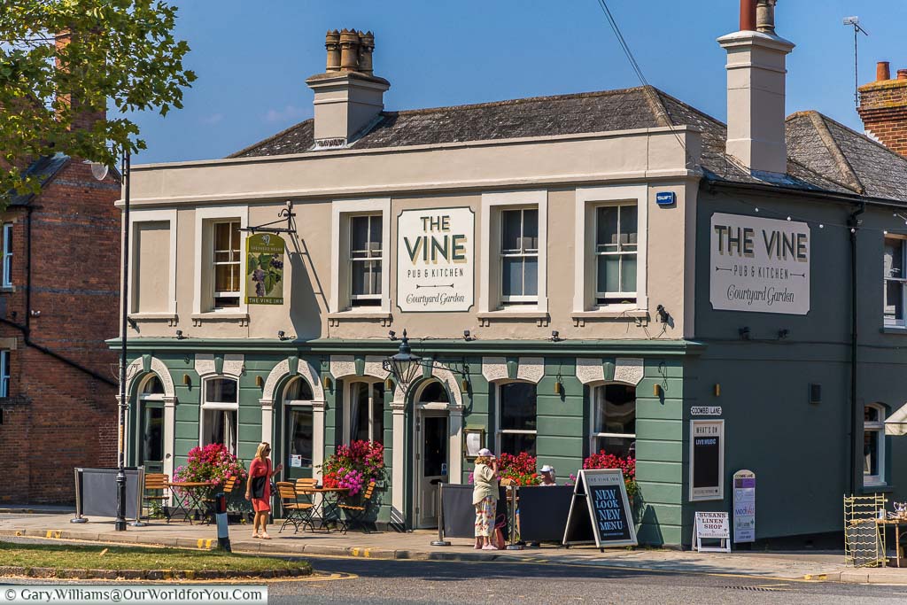 The Vine pub on the High Street freshly painted in a green and cream colour scheme. Decorated with flower arrangements and tables and chairs outside.