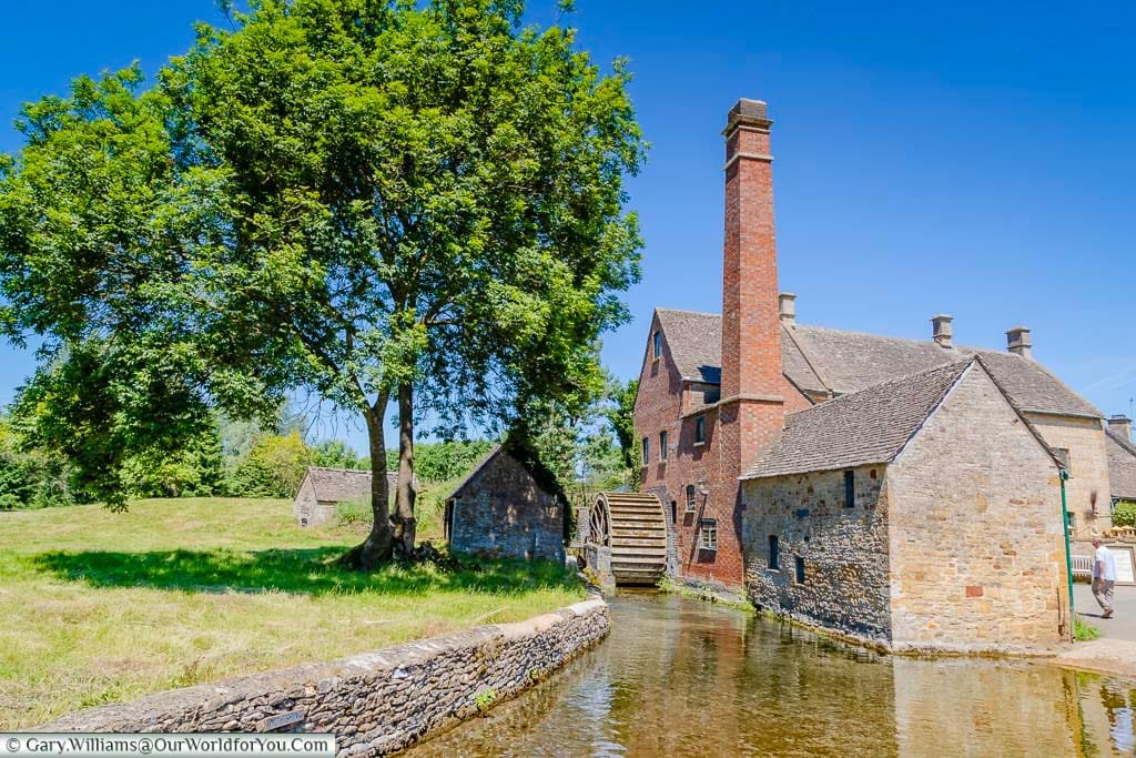 An idyllic Cotswold scene of the watermill in Lower Slaughter under a deep blue sky