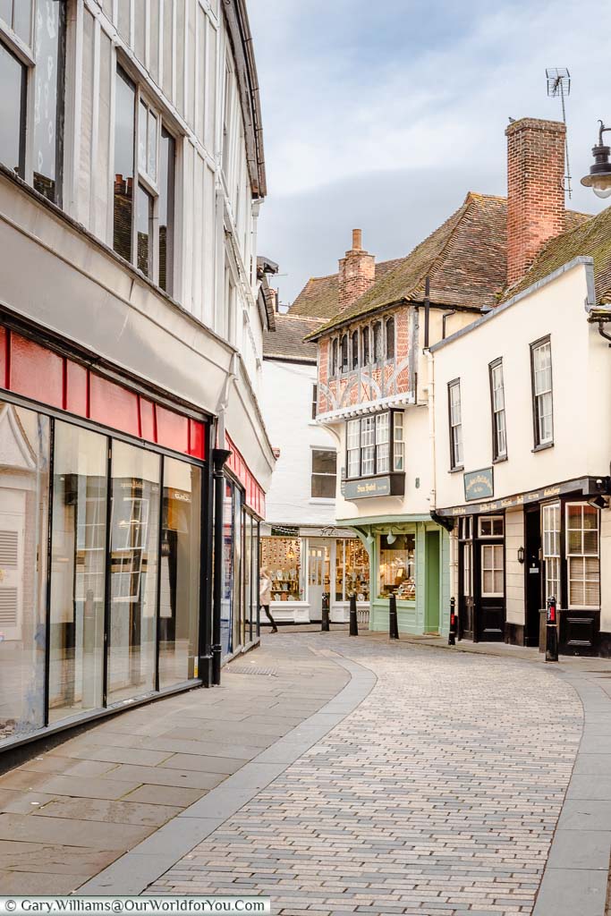 A view along a quiet cobbled lane in Canterbury towards a historic building that was once home to Charles Dickens and is now a jewellers.