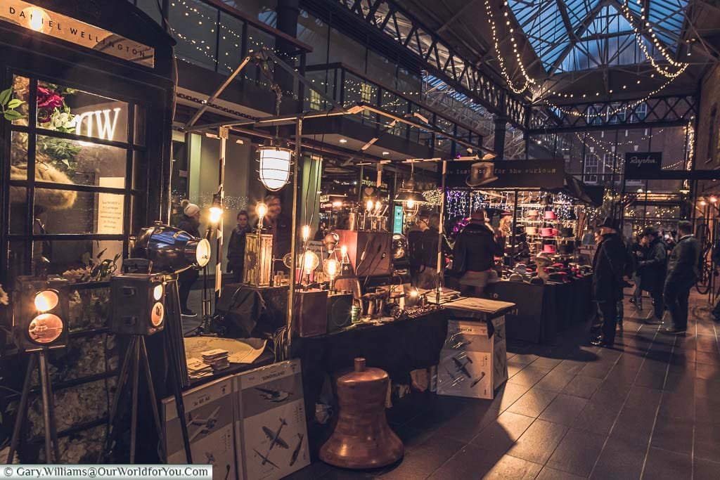 Stalls in Spitalfields market selling unique Christmas gifts. The 2 stalls in shot are focusing on lamps and hats.