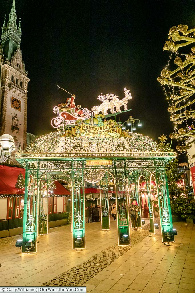 The decorative illuminated entrance gates to Hamburg's Weihnachtsmarkt Christmas market at night with the Rathaus tower in the edge of the shot.