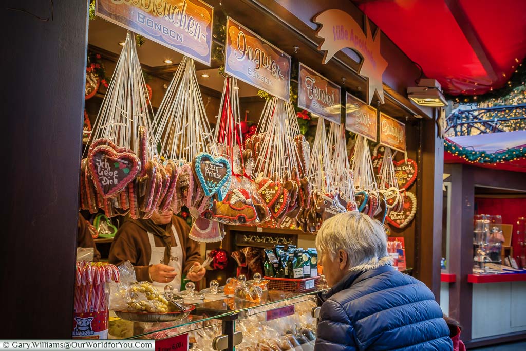 A woman inspecting the gingerbread at a Christmas market stall in Cologne. The display is full of hanging iced gingerbread hearts.