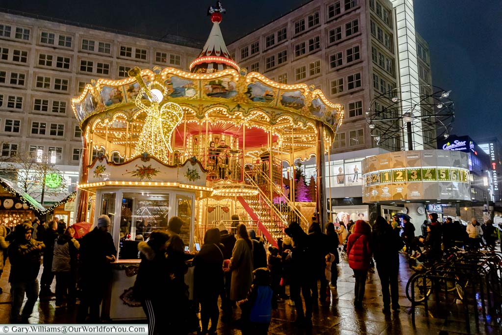 An illuminated double-height carousel in front of the world clock at Alexanderplatz Christmas Market in Berlin.