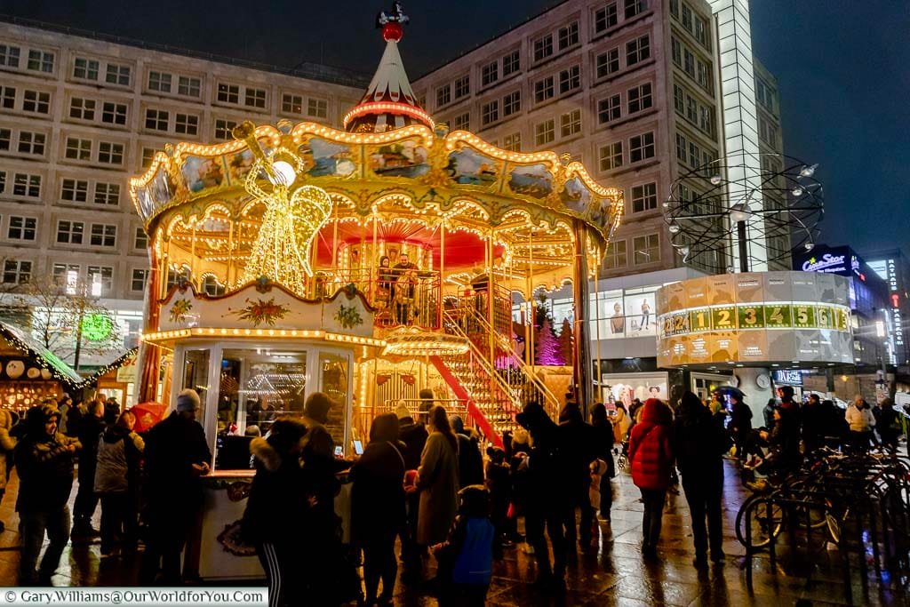 An illuminated double-height carousel in front of the world clock at Alexanderplatz Christmas Market in Berlin.