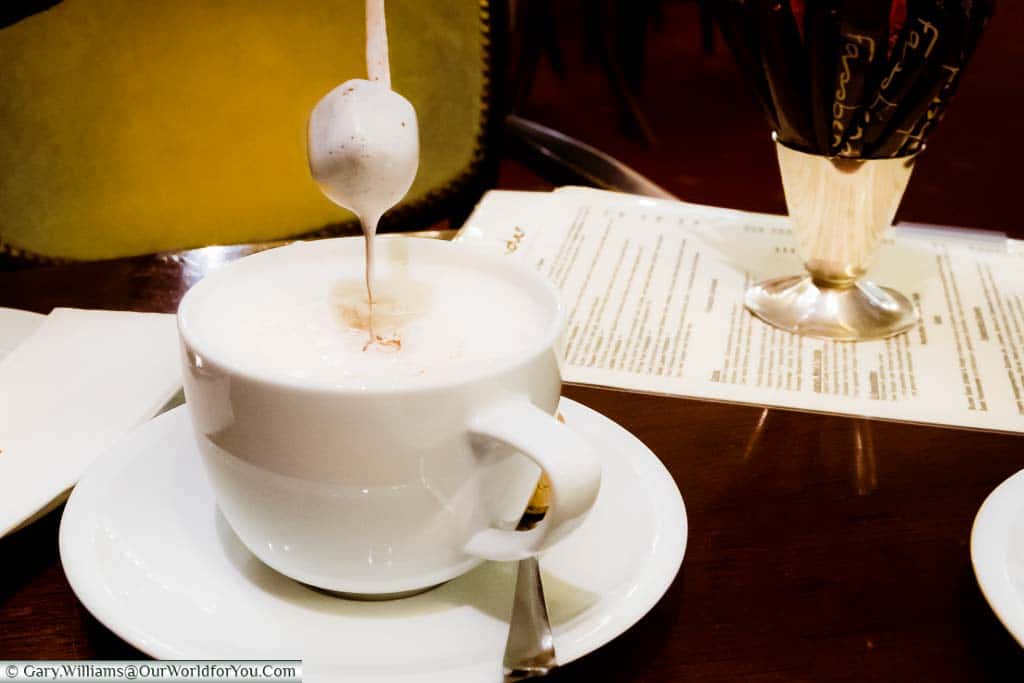 A cube of melting chocolate on a skewer being drizzled into a white cup of hot milk to create your own hot chocolate in Fassbender's Cafe in Cologne.