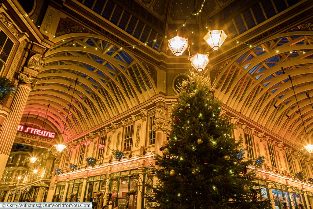 Inside the centre of Leadenhall Market at dusk, underneath the historic iron roof of this fabulous space. The Christmas tree take centre stage under 3 bright Victorian lamps.