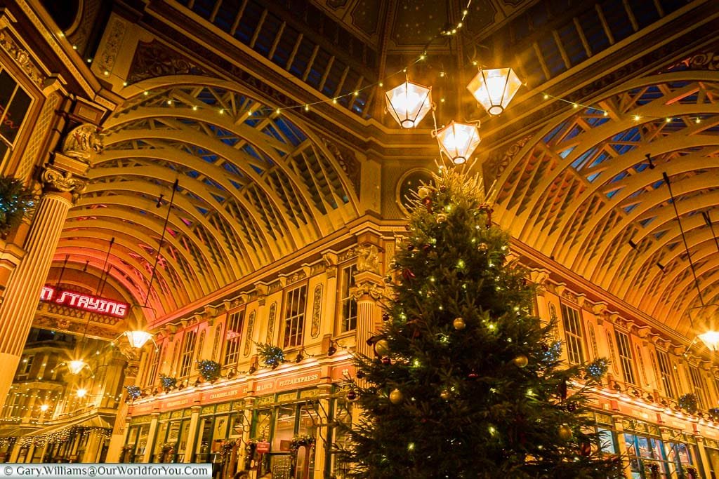 Inside the centre of Leadenhall Market at dusk, underneath the historic iron roof of this fabulous space. The Christmas tree take centre stage under 3 bright Victorian lamps.