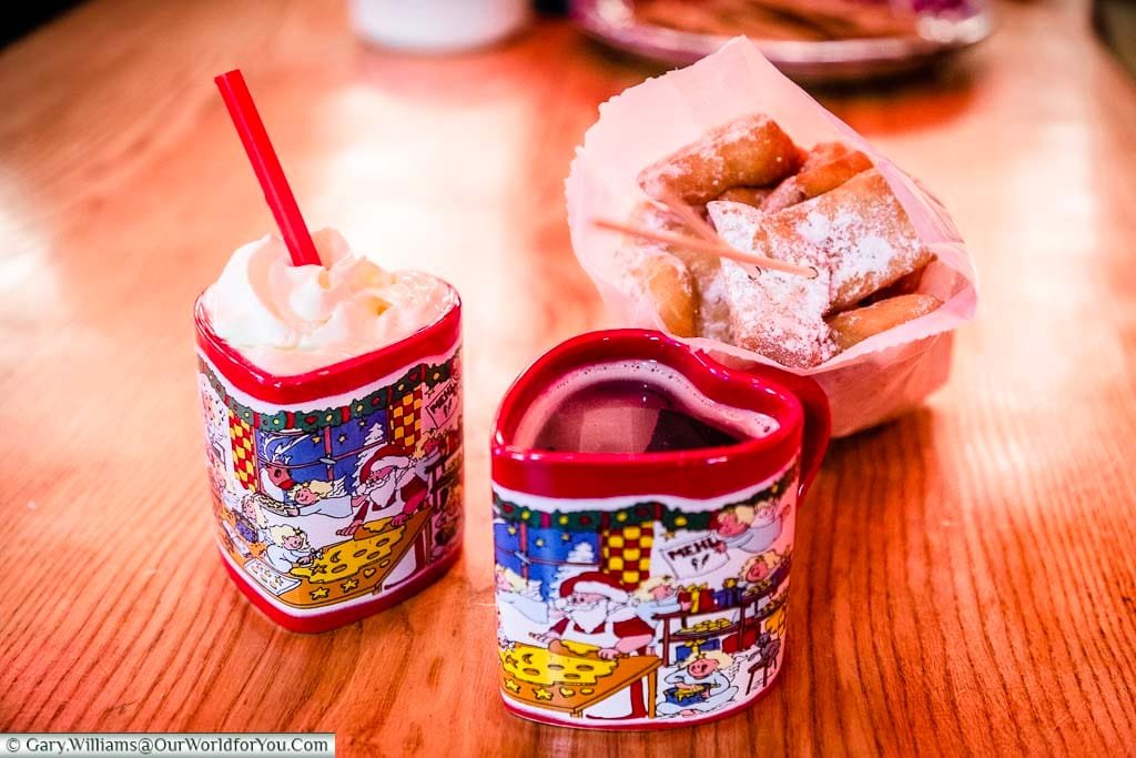 Heart-shaped Christmas mugs and a bag of little mini doughnut style treats dusted with icing sugar on a bench in Bremen's Christmas Markets.