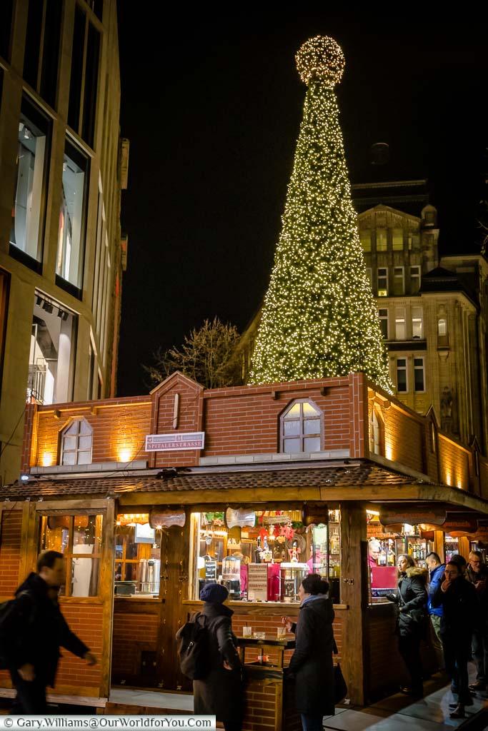 A large illuminated Christmas tree behind a stall in Hamburg's Spitalerstraße Christmas Market