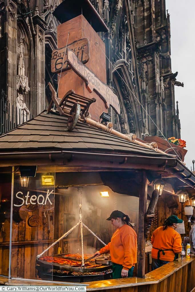 A meat stall with an open smokey grill advertising 'steak' at a Cologne Christmas Market stall