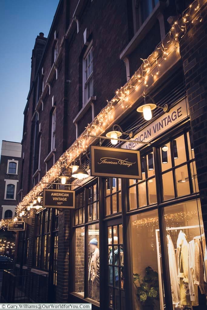 The American Vintage store at Spitalfields market at dusk. The store has some decorative festive lights complementing the golden tones of the image.