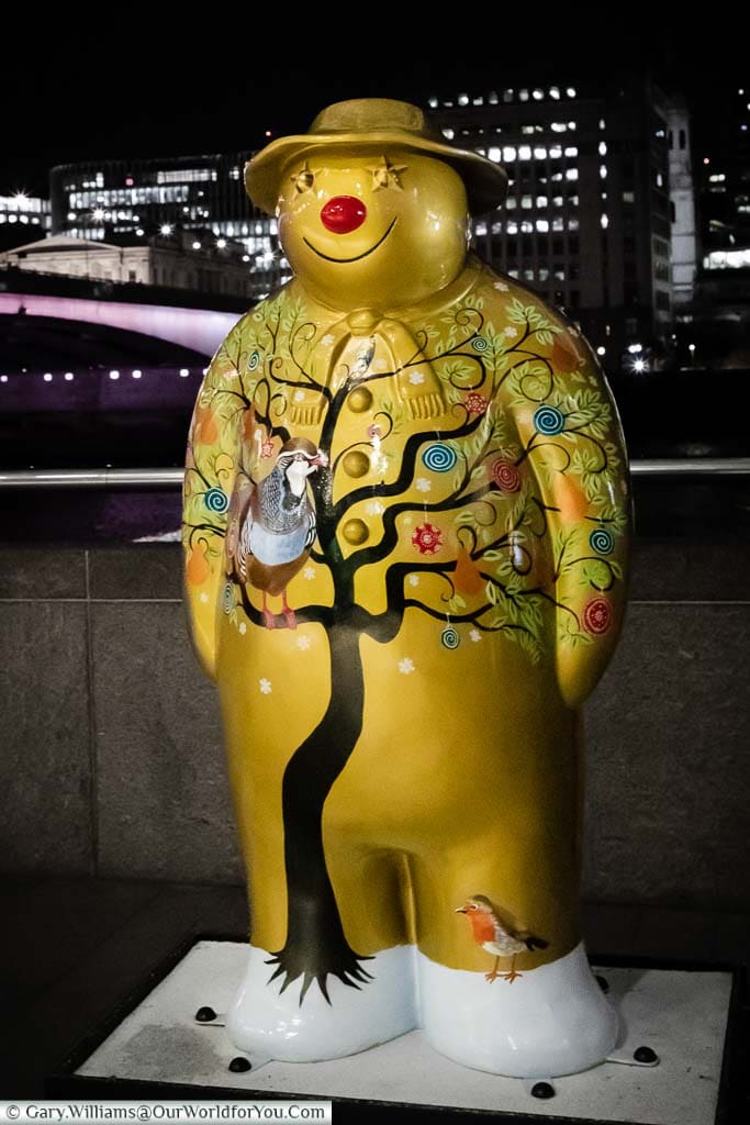 A life-size statue of Raymond Briggs ‘The Snowman’ decorated to depict the first. day of Christmas on the banks of the River Thames with London Bridge in the background.