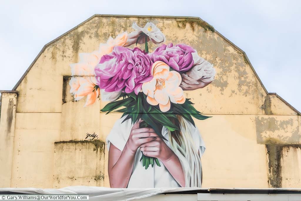 A mural of a woman holding a large bouquet of flowers in front of her face on the side of a building in Bristol