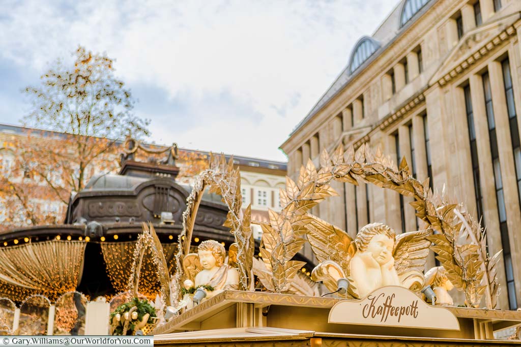 Angel decorations, trimmed in gold, on the huts of the Angel market in Düsseldorf with the aged bronze roof of the bandstand in the centre of Heinrich-Heine-Platz in the background.